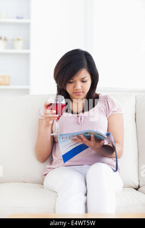 Femme assise sur un canapé et est titulaire d'un magazine Banque D'Images