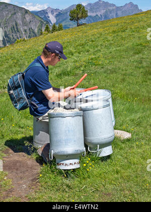 Un homme jouant des bidons de lait renversé comme batterie dans une prairie alpine suisse. Banque D'Images