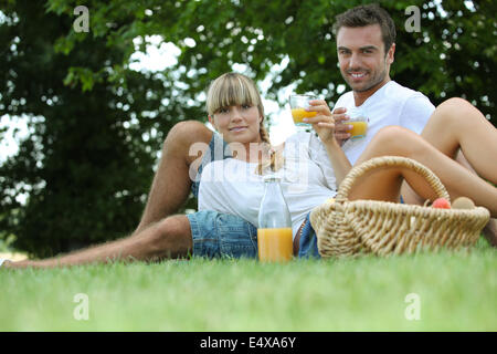 Couple drinking orange juice dans un parc Banque D'Images