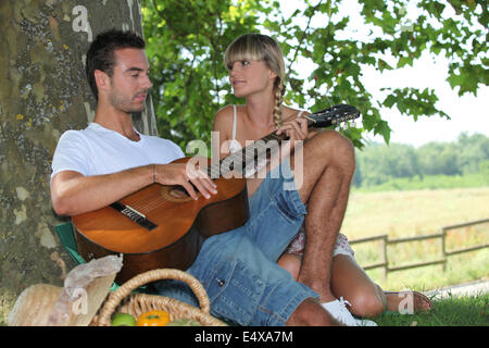 Jeune couple avec panier pique-nique assis par tree Banque D'Images