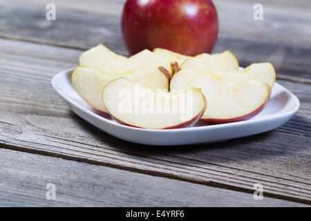 Photo horizontale de tranches de pommes fraîches, sur plaque blanche, avec pomme entière et bois rustique en arrière-plan Banque D'Images