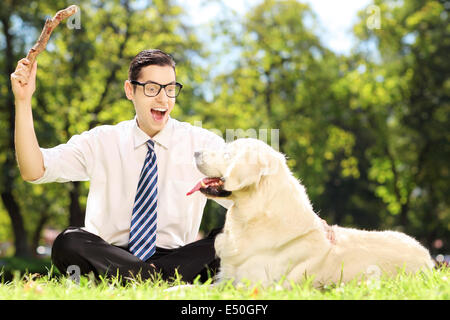 Guy avec cravate et lunettes assis sur une herbe jouer avec le labrador retriver chien dans un parc Banque D'Images