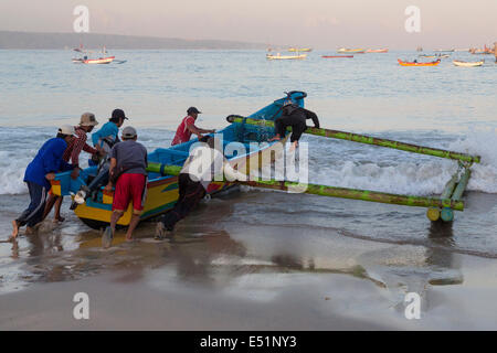 Jimbaran, Bali, Indonésie. Les pêcheurs de lancer un bateau, tôt le matin. Banque D'Images