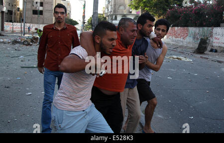 La ville de Gaza, Territoires palestiniens. 18 juillet, 2014. Gaza, bande de Gaza, Territoires palestiniens. 18 juillet, 2014. Les hommes palestiniens aider un journaliste local qui s'est blessé au cours d'un bombardement israélien sur un bâtiment de bureaux hébergeant plusieurs médias dans la ville de Gaza, 18 juillet 2014. Credit : ZUMA Press, Inc./Alamy Live News Banque D'Images