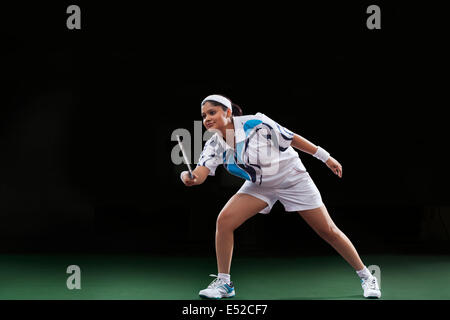 Jeune femme dans les vêtements de sport jouer au badminton sur fond noir Banque D'Images