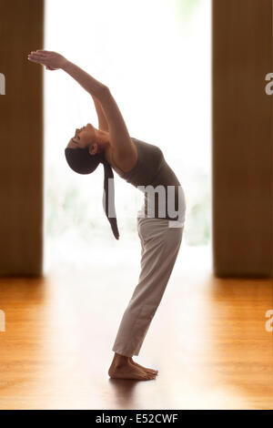 Photo de profil young woman doing back bend yoga pose sur plancher en bois Banque D'Images