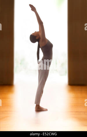 Photo de profil young woman doing back bend yoga pose sur plancher de bois franc Banque D'Images