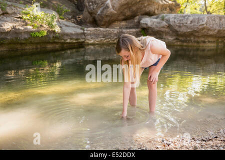 Une jeune fille se penchant pour mettre sa main dans l'eau peu profonde. Banque D'Images