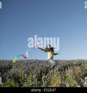 Un enfant, une fille courir avec un streamer papier voltigeant dans le vent. Banque D'Images