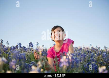 Une jeune fille assise dans un champ de fleurs sauvages, de rire. Banque D'Images