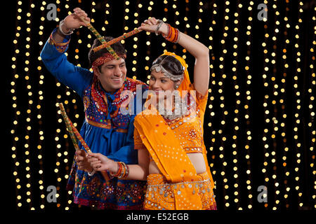 Un couple indien traditionnel dans l'exécution d'usure Dandiya Raas contre néons Banque D'Images