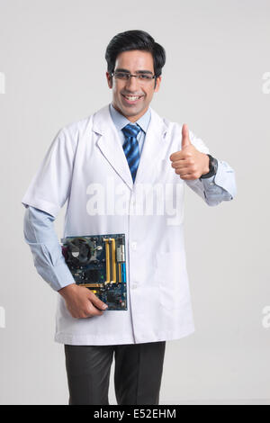 Portrait of male technician gesturing Thumbs up en maintenant le conseil de mère sur fond gris Banque D'Images