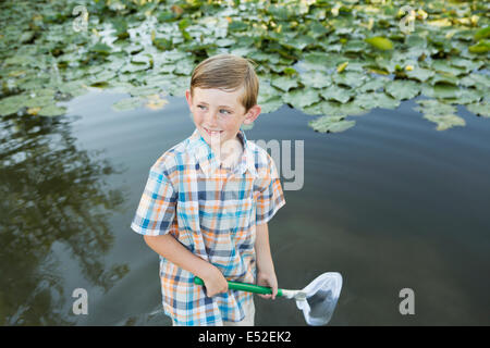 Un jeune garçon debout dans l'eau peu profonde avec un filet de pêche. Banque D'Images