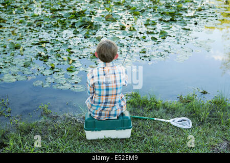 Vue arrière d'un jeune garçon assis sur son baitbox, pêche dans la rivière. Banque D'Images