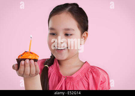 Petite fille tenant un petit gâteau avec une bougie Banque D'Images