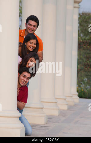 Portrait of smiling friends peeking de derrière la colonne à l'extérieur Banque D'Images