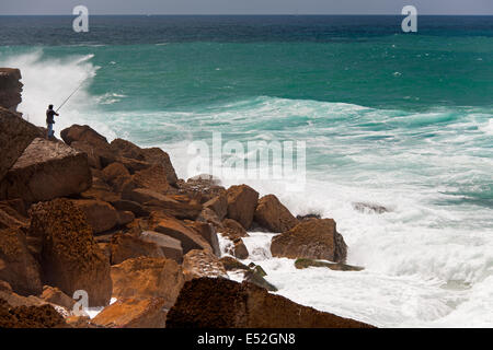 Un pêcheur debout sur les rochers surf casting dans le livre blanc sur les vagues Antlantic côte. Banque D'Images
