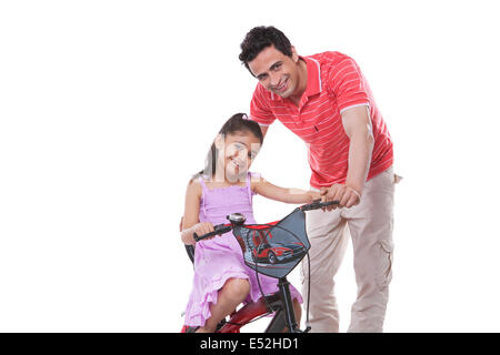 Portrait de père en fille aider équitation vélo contre fond blanc Banque D'Images