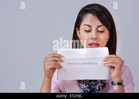 Young businesswoman holding enveloppe confidentielle contre l'arrière-plan gris Banque D'Images