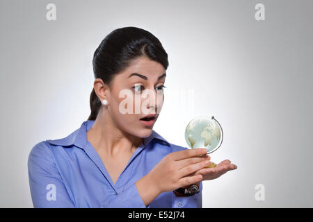 Surpris businesswoman looking at globe de cristal sur fond gris Banque D'Images