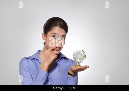 Thoughtful Indian businesswoman holding globe sur fond gris Banque D'Images