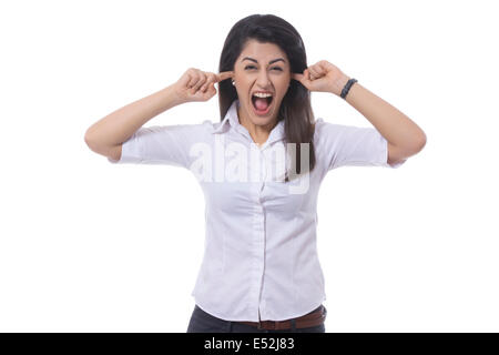 Portrait de femme frustrée avec les doigts dans les oreilles des cris contre fond blanc Banque D'Images