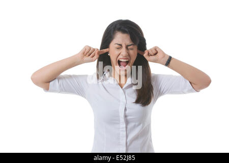 Frustrated businesswoman avec les doigts dans les oreilles en criant sur fond blanc Banque D'Images