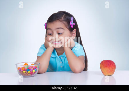 Fille confus le choix entre un aliment sucré et apple contre fond bleu Banque D'Images