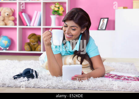 Happy young woman using digital tablet while drinking coffee at home Banque D'Images