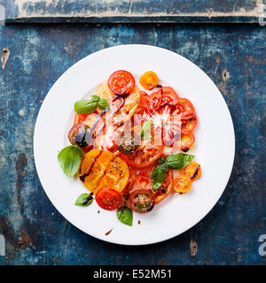 Frais salade de tomates mûres colorés avec de l'huile d'olive et de vinaigre balsamique sur fond de bois bleu Banque D'Images