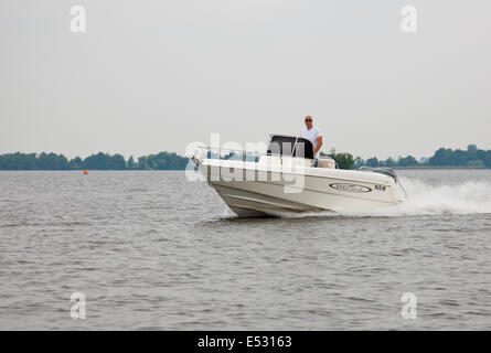 Un homme à la tête chauve avec des lunettes de soleil au volant de son bateau de vitesse à Loosdrecht, Hollande. Banque D'Images