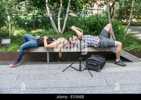 Jeune couple de touristes de prendre une pause pour vérifier leurs photos sur un banc de parc High Line ombragé par le feuillage d'été luxuriant Manhattan Banque D'Images