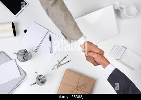 Deux hommes atteignant plus d'un bureau pour serrer la main. Tourné à partir d'un angle élevé le bureau est blanc comme le sont la plupart des articles de bureau à l'exception des Banque D'Images