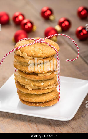 Une pile de beurre de cacahuète cookies faits maison remplie avec ornements rouge en arrière-plan Banque D'Images