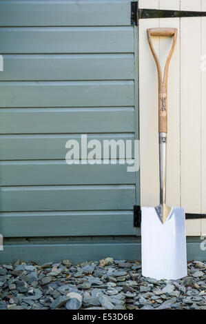 Pelle en acier inoxydable appuyé contre un abri de jardin en bois. Banque D'Images