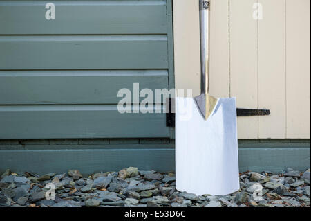 Pelle en acier inoxydable appuyé contre un abri de jardin en bois. Banque D'Images