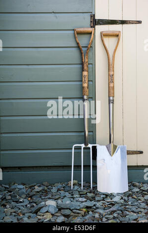 Fourche à bêcher et spade appuyé contre un hangar peint Banque D'Images