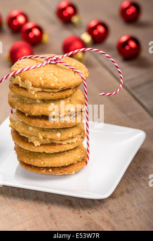 Une pile de beurre de cacahuète cookies faits maison remplie avec ornements rouge en arrière-plan Banque D'Images