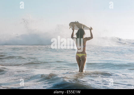 Jeune femme surfer carrying surfboard on head à marcher vers le fracas des vagues Banque D'Images