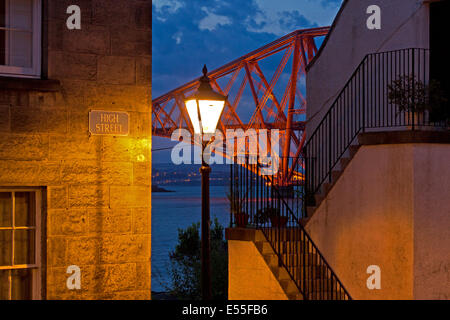 Une photo de la Forth Rail Bridge à travers une lacune dans la rue principale pavée à South Queensferry au crépuscule. Banque D'Images