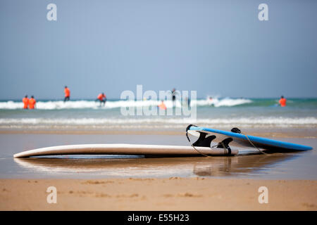 Groupe de personnes ayant des leçons de surf entre les vagues sur une plage de sable fin de l'Espagne et des planches en premier plan ciel bleu en arrière-plan Banque D'Images