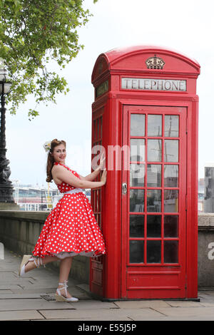 Fille en robe rouge à pois debout à côté de phone box Banque D'Images