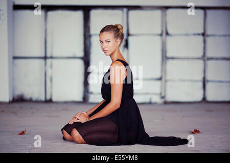 Jeune femme en robe noire à genoux sur le sol Banque D'Images