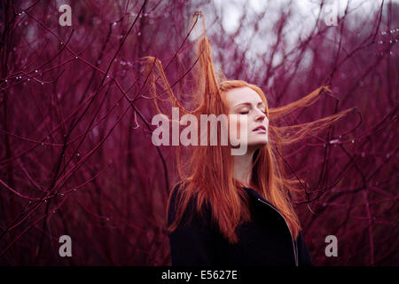 Femme aux longs cheveux rouges entre les branches, portrait