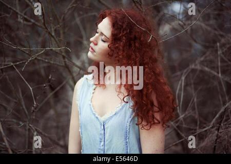 Femme aux longs cheveux rouges entre les branches, portrait Banque D'Images