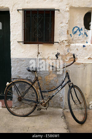 Vieux Vélo enchaîné à un cadre de fenêtre contre un mur dans une rue espagnole : Ciutadella, Menorca, Espagne. Banque D'Images