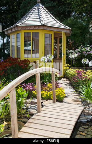 Pont voûté en bois sur l'eau du jardin à Tatton Park, Manchester, Royaume-Uni.Juillet 2014.The Water Garden & Gazebo ; Médaille d'argent à l'événement sur le thème du carnaval RHS - Royal Horticultural Society à Tatton Park. Banque D'Images