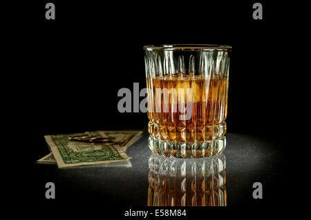 Photographie d'un verre de whisky à côté de billets et pièces de monnaie dollar trimestre. Banque D'Images