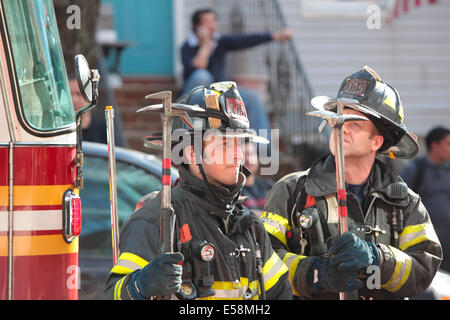 Les pompiers FDNY stand by avec des outils en ligne de combat quartier résidentiel maison en feu Banque D'Images
