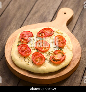 Du pain fait maison composé d'une pâte levée garnie de tranches de tomate, l'ail et les feuilles de thym servi sur planche de bois Banque D'Images